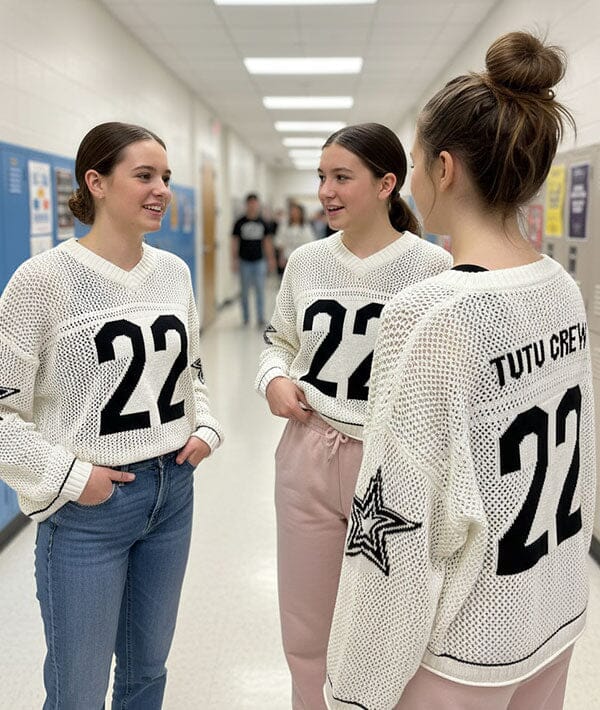 Three women wearing white sweaters with the number 22 in a school hallway.