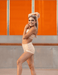 Woman in a beige bikini standing against an orange wall.