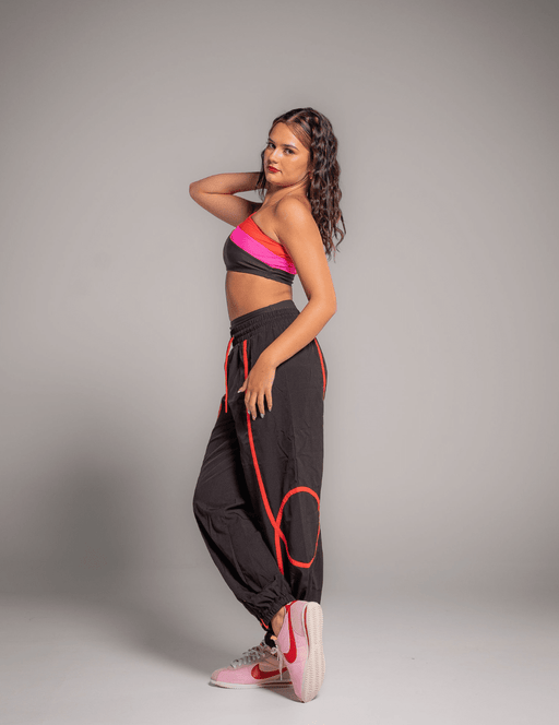 Woman wearing a pink top and black pants with red accents against a gray background