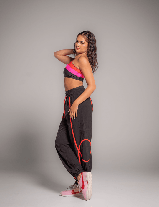 Woman wearing a pink top and black pants with red accents against a gray background