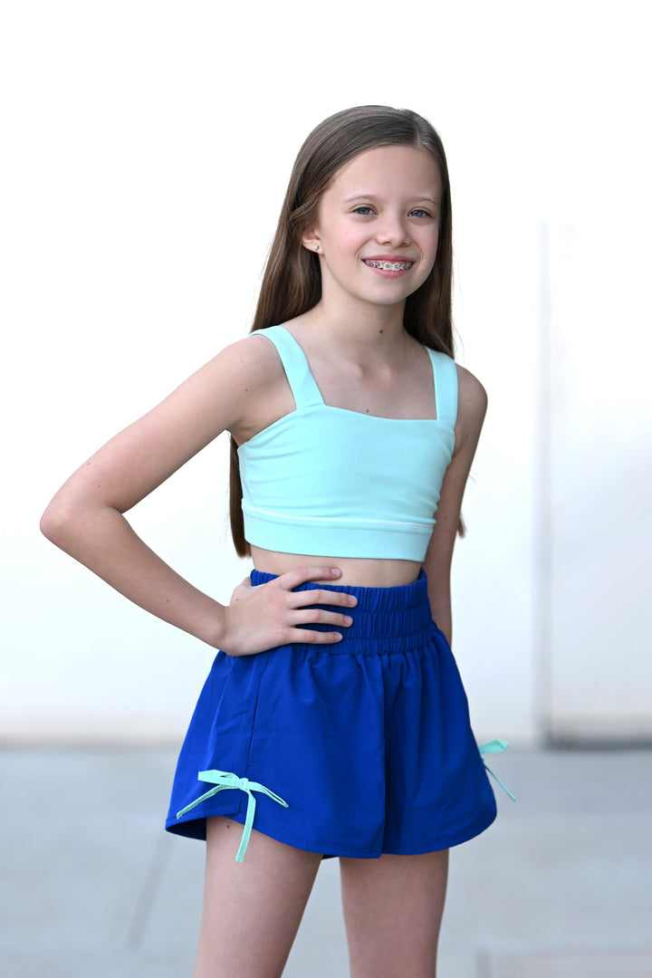 Young girl wearing a light blue crop top and blue skirt on a white background