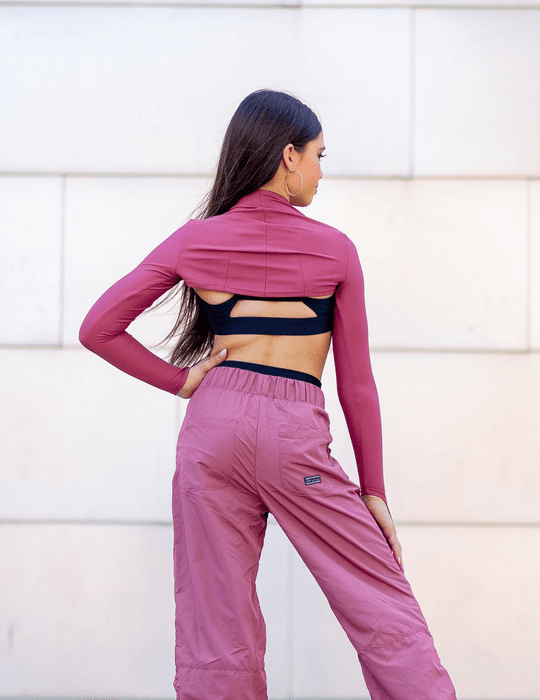 Woman wearing a pink athletic outfit with a black sports bra against a white wall.