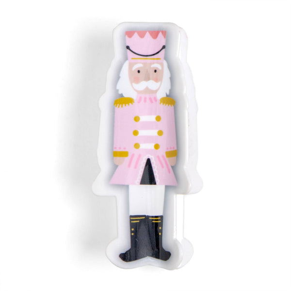 A decorative white plastic mold or tray shaped like a nutcracker soldier, featuring a pink uniform, gold buttons and epaulets, white beard and pants, and black boots, shown on a plain white background.