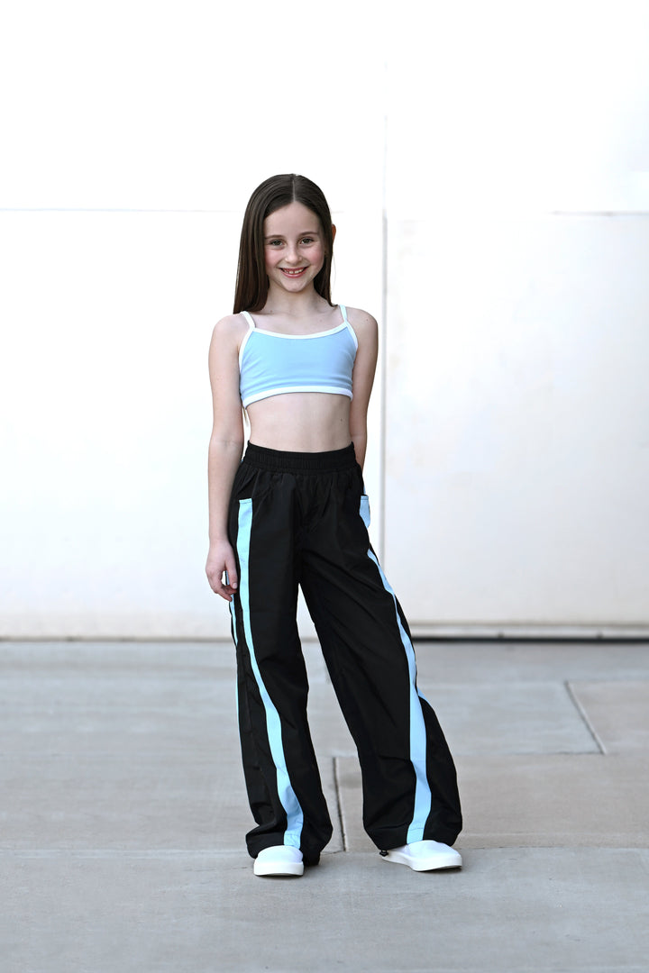 Young girl wearing a light blue crop top and black pants with blue stripes on a white background