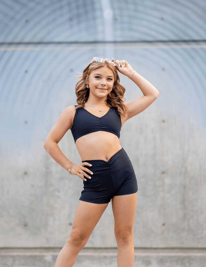 Young woman in black athletic wear posing against a gray wall.