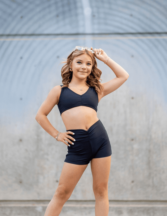 Young woman in black athletic wear posing against a gray wall.