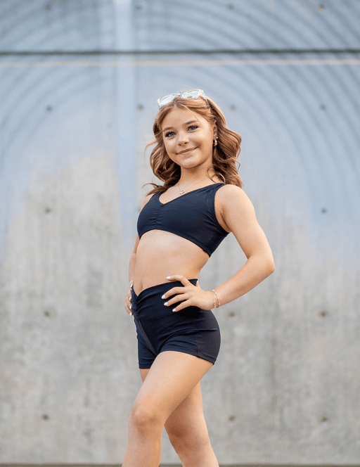 Young girl in black athletic wear standing against a gray wall.