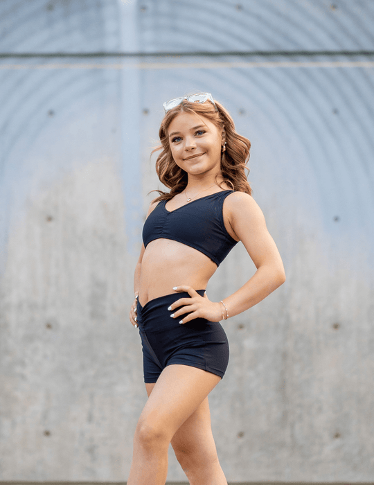 Young girl in black athletic wear standing against a gray wall.