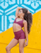 Woman in maroon athletic wear posing against a colorful geometric background