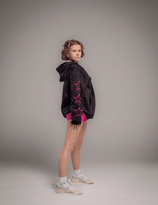 Person wearing a black hoodie with pink star designs on a gray background