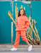 Person wearing an orange tracksuit standing in front of a teal wall with cacti.