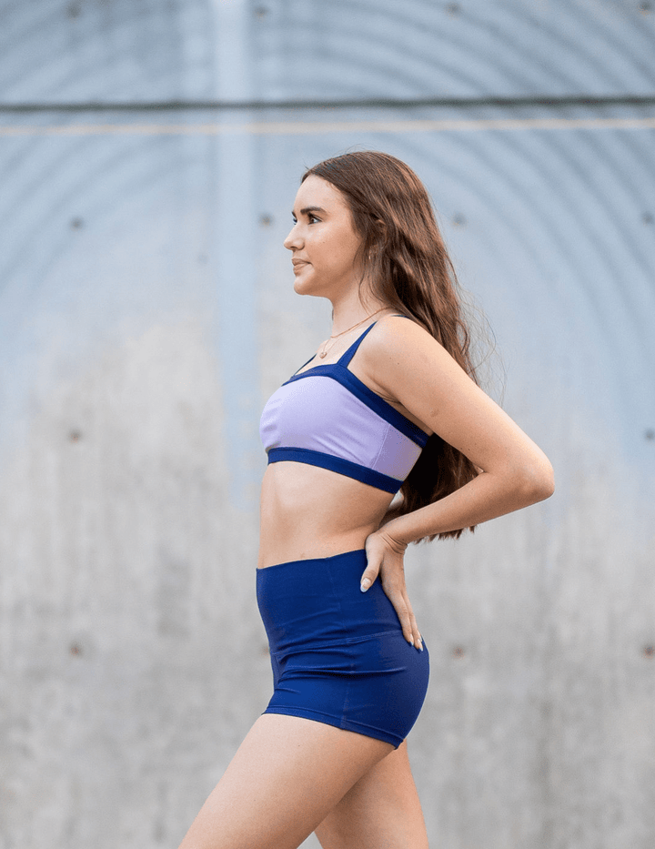 Woman wearing a blue and purple sports bra and shorts set against a gray background