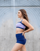 Woman wearing a blue and purple sports bra and shorts set against a gray background