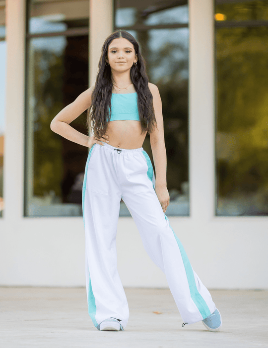 Person wearing a turquoise top and white pants with blue accents outdoors.