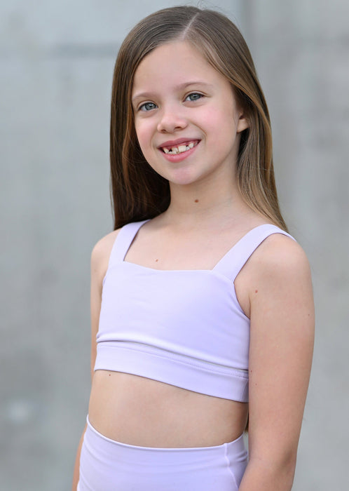 Young girl wearing a light purple sports bra and shorts against a neutral background