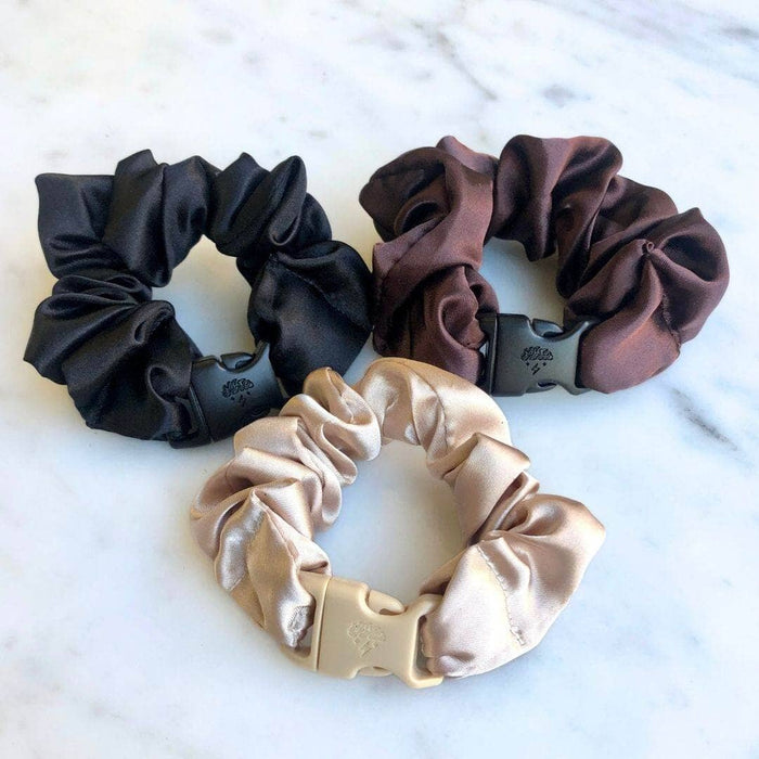 Three satin scrunchies in black, brown, and beige on a marble surface.