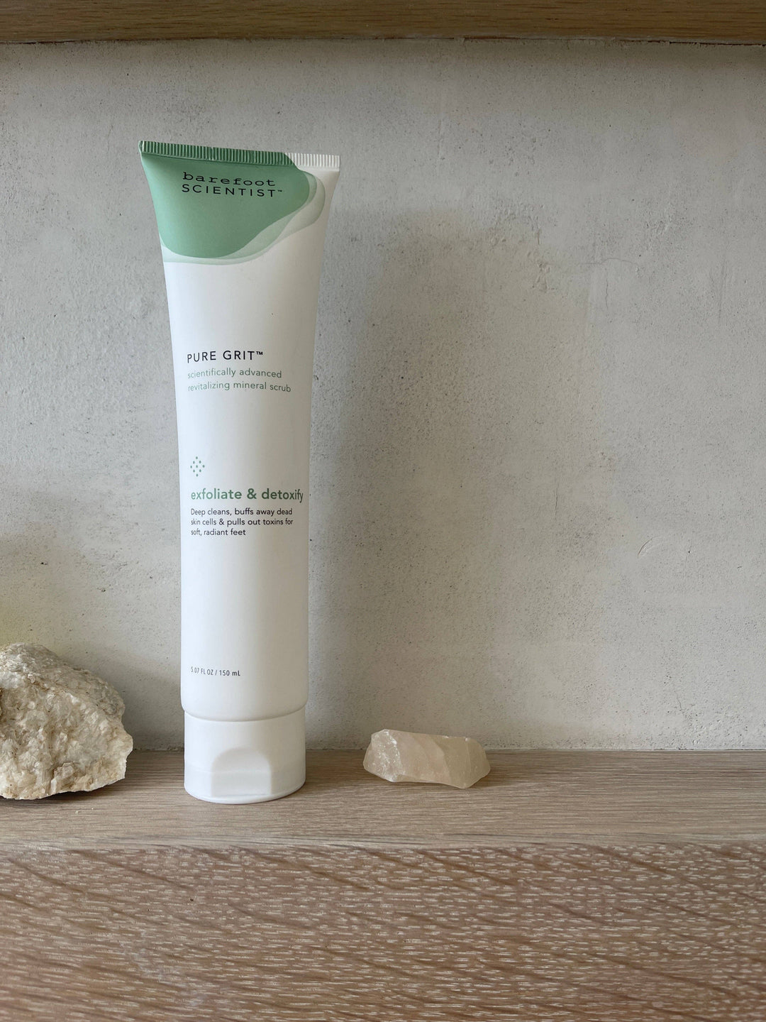 Tube of 'Pure Grit' skincare product on a wooden surface with a stone background