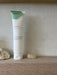 Tube of 'Pure Grit' skincare product on a wooden surface with a stone background