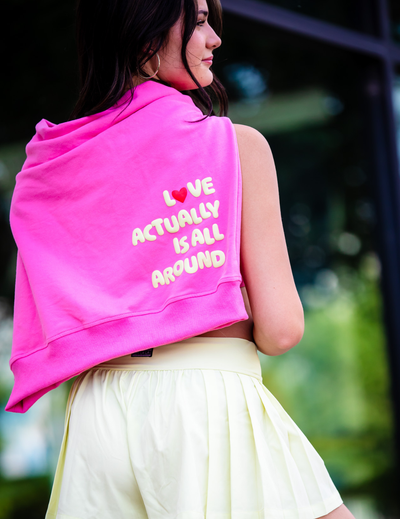 Person wearing a pink hoodie with text on the back, standing outdoors.