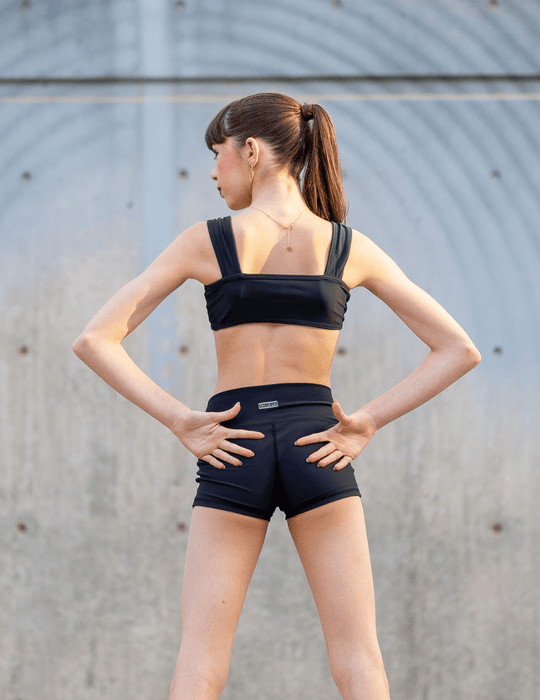 Woman wearing a black sports bra and shorts against a gray wall.