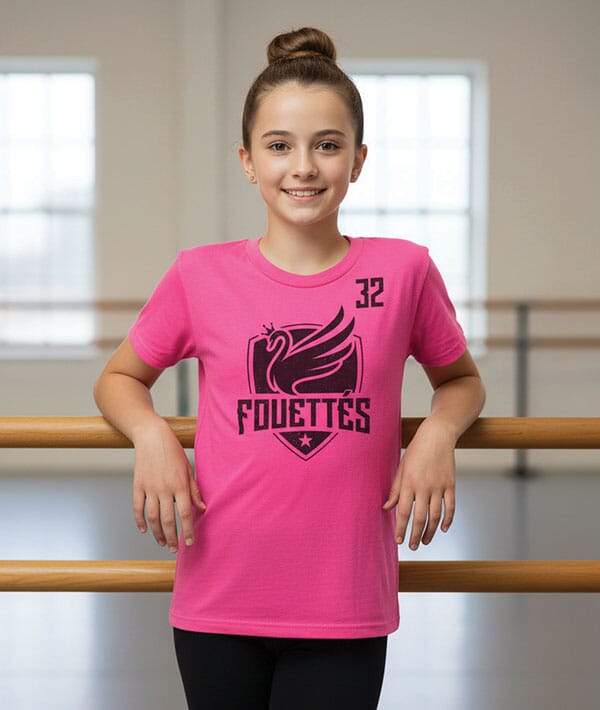 Young girl wearing a pink t-shirt with 'Fouettes' logo in a dance studio.