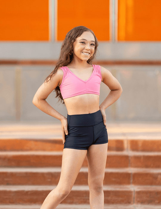 Woman in pink sports bra and black shorts standing on steps with an orange wall in the background