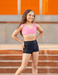 Woman in pink sports bra and black shorts standing on steps with an orange wall in the background