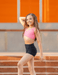 Young girl in a pink top and black shorts standing on steps with an orange wall in the background