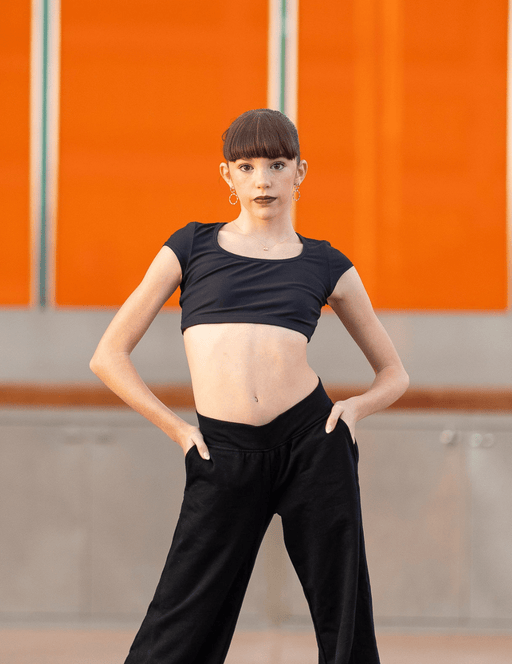 Person wearing a black crop top and black pants against an orange wall.
