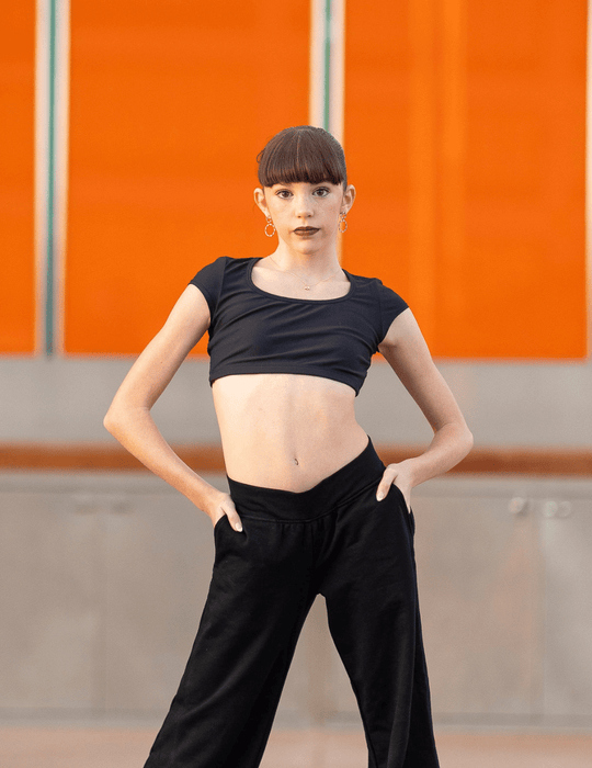 Person wearing a black crop top and black pants against an orange wall.