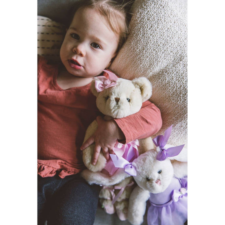 Child holding two teddy bears with ribbons in a cozy setting