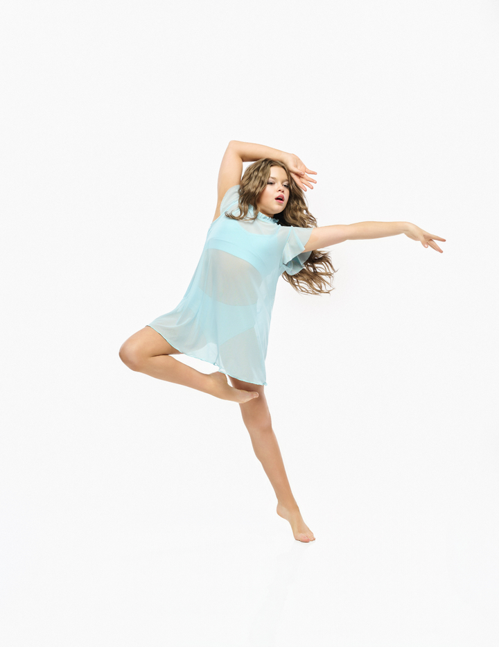 A woman in a flowing light blue sheer dress poses dynamically against a seamless white background.
