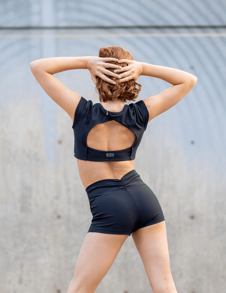 Person wearing a black sports bra and shorts with a visible brand logo, standing against a gray wall.