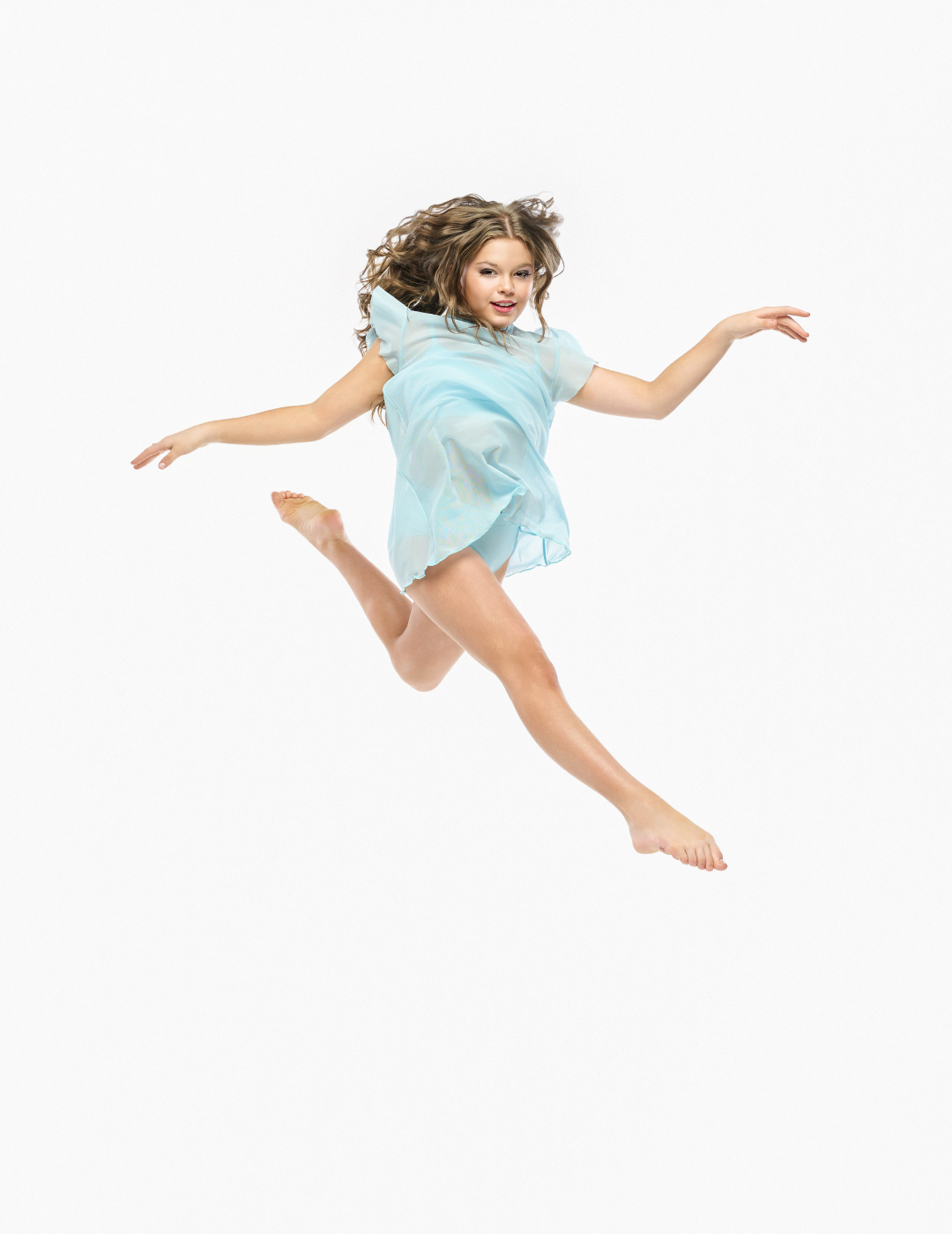 A young girl with curly brown hair is captured mid-air, jumping in a joyful pose while wearing a light blue, semi-sheer tulle dress against a solid white background.