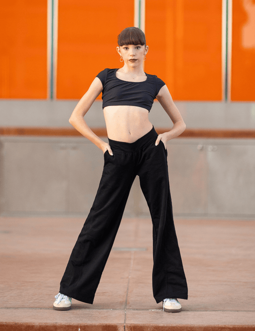 Person wearing a black crop top and wide-leg pants standing against an orange wall.