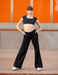 Person wearing a black crop top and wide-leg pants standing against an orange wall.