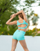Woman in turquoise athletic wear stretching outdoors with a blurred natural background