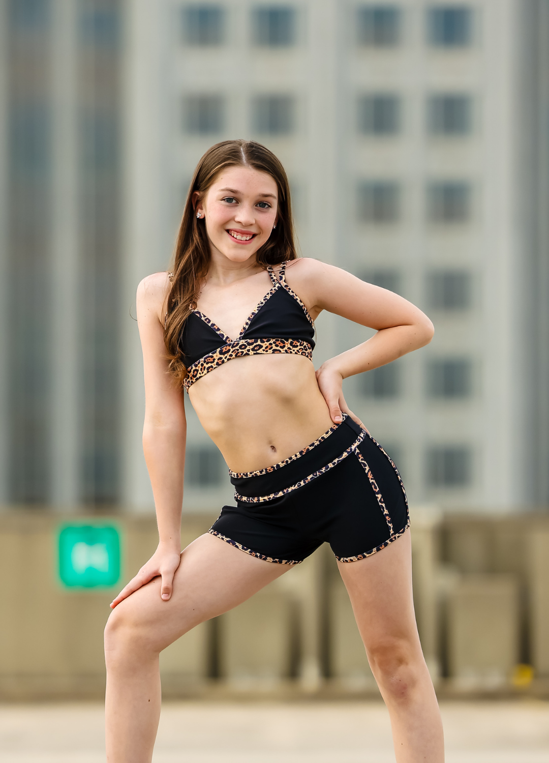 Woman in black and leopard print outfit posing outdoors with buildings in the background
