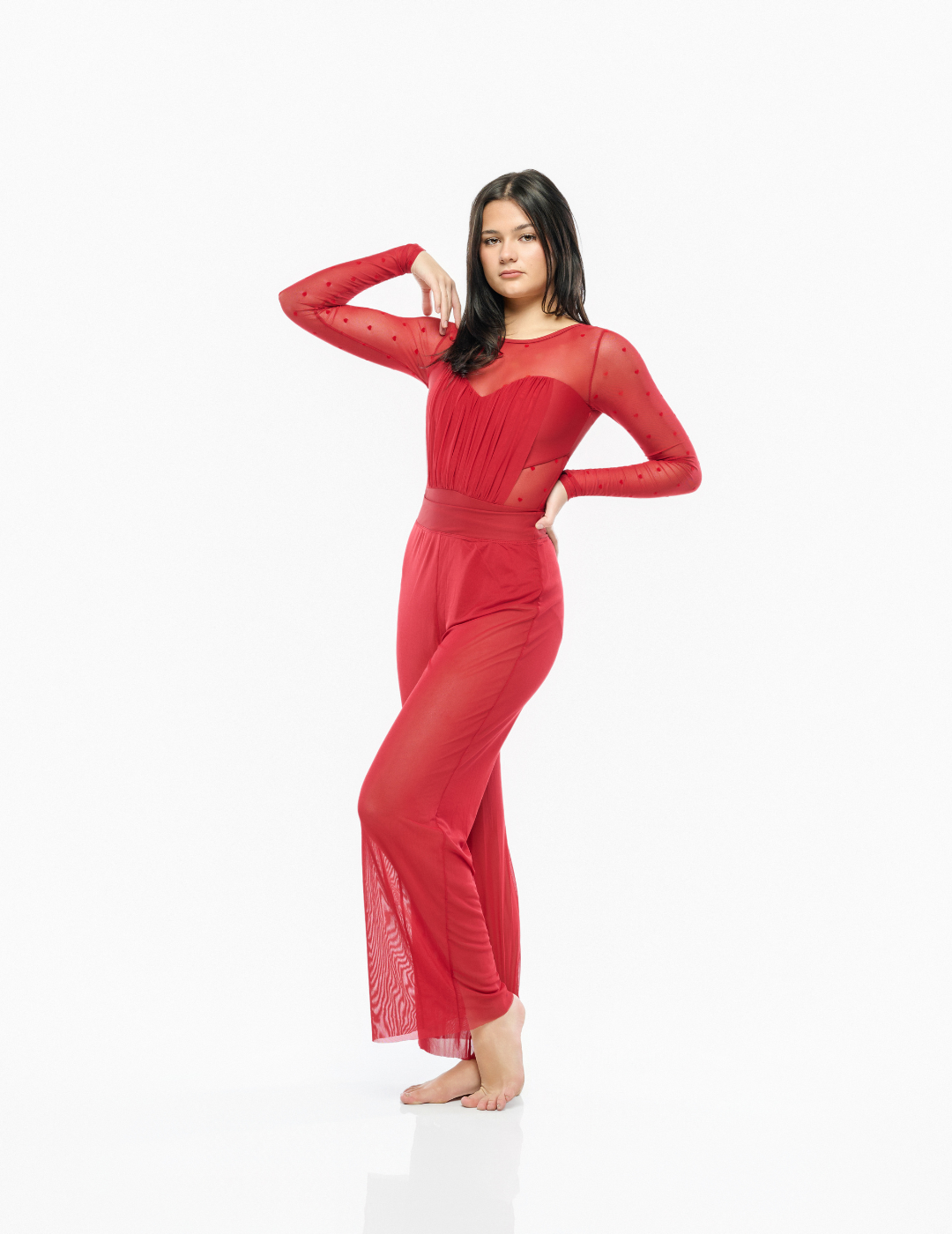 A woman modeling a long-sleeve red sheer mesh dress with a fitted waist and flared legs, posed against a seamless white studio background.