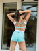 Woman wearing a turquoise sports bra and shorts set outdoors.