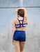 Woman wearing a blue sports bra and shorts against a gray wall.