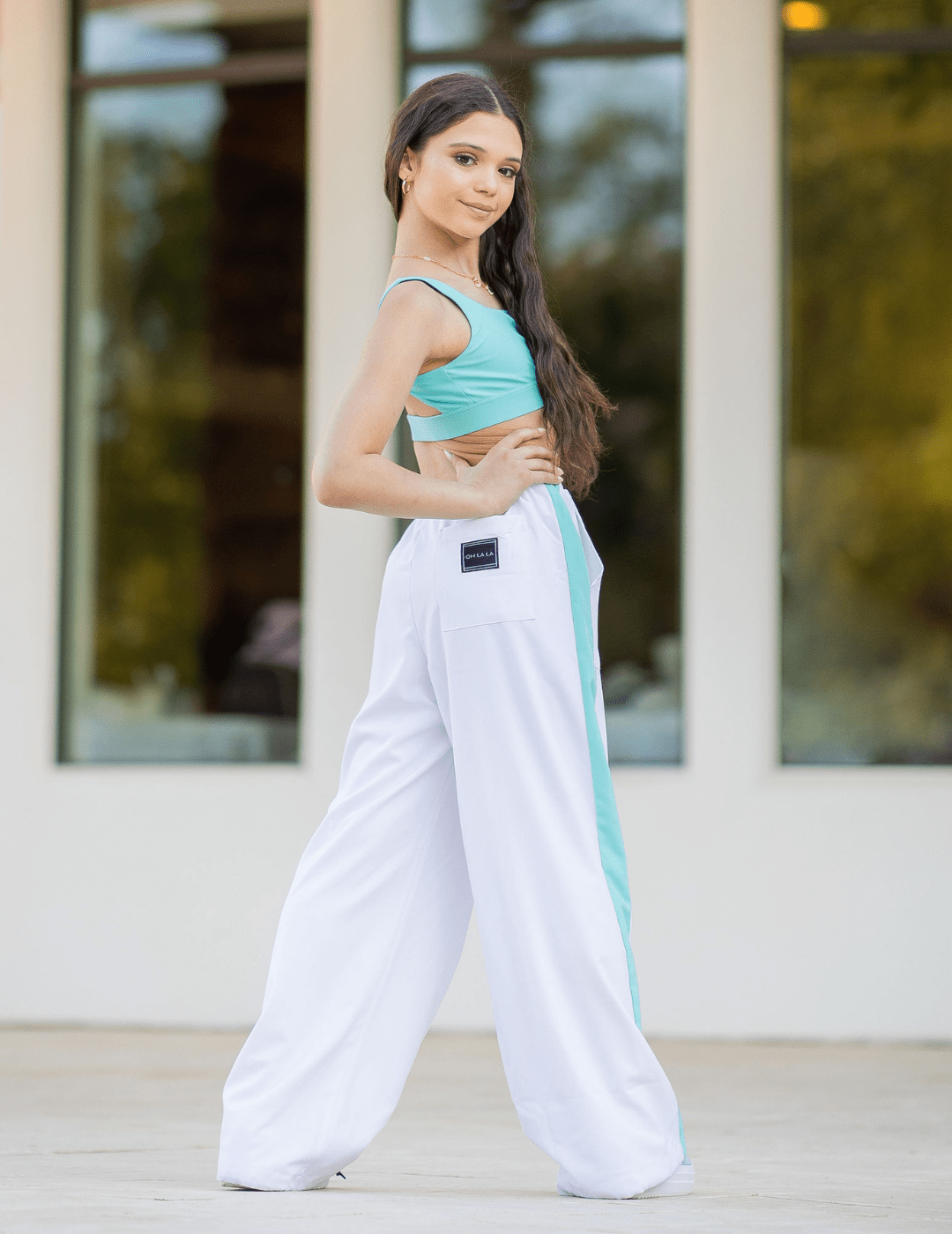 Woman wearing a turquoise sports bra and white pants with a blue stripe outdoors.