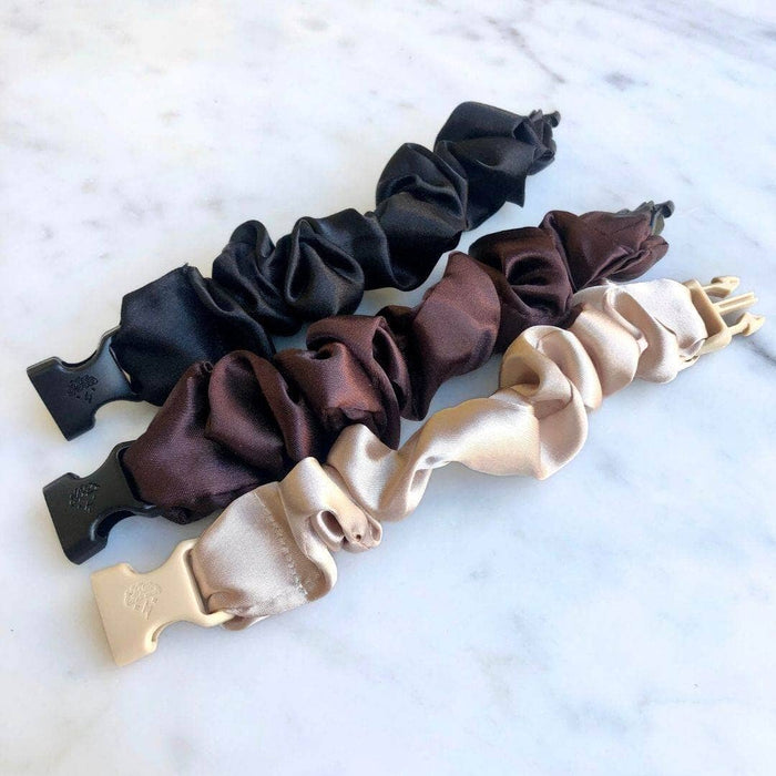 Set of three satin scrunchies in black, brown, and beige on a marble surface.