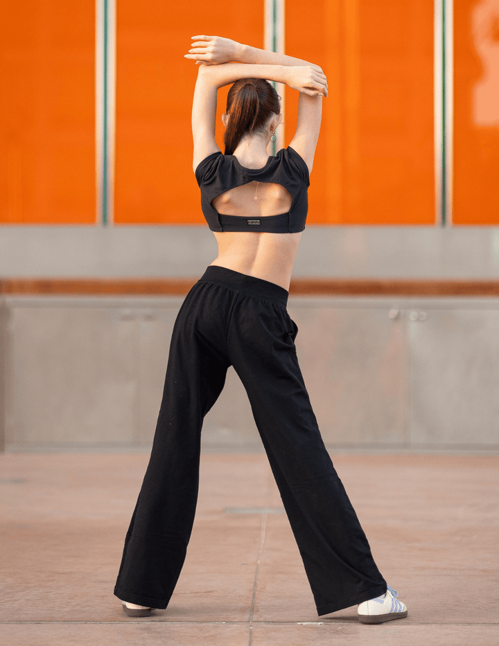 Person wearing a black athletic outfit stretching against an orange wall.