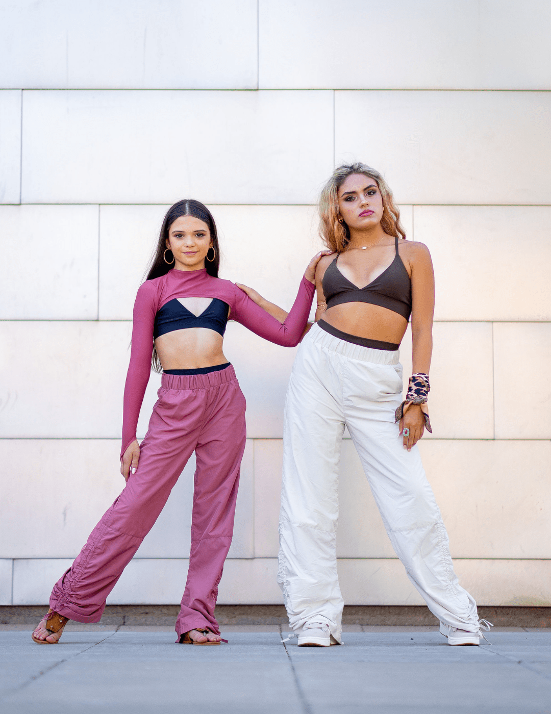 Two women posing together against a light-colored wall.
