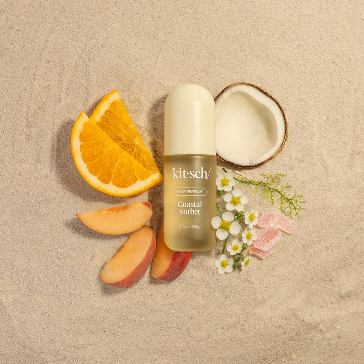 Kit-sch Coastal Sorbet perfume bottle surrounded by fruit slices and flowers on a beige background