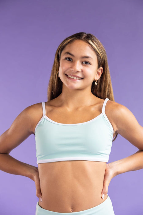 Young girl wearing a light blue sports bra and shorts on a purple background