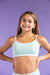 Young girl wearing a light blue sports bra and shorts on a purple background