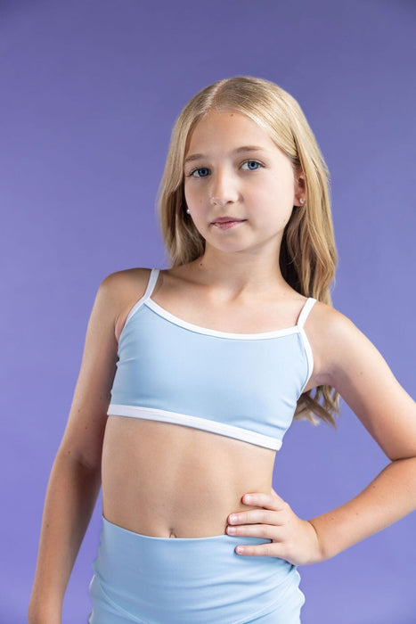 Young girl wearing a light blue sports bra and shorts against a purple background