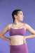 Woman wearing a purple sports bra and leggings against a purple background